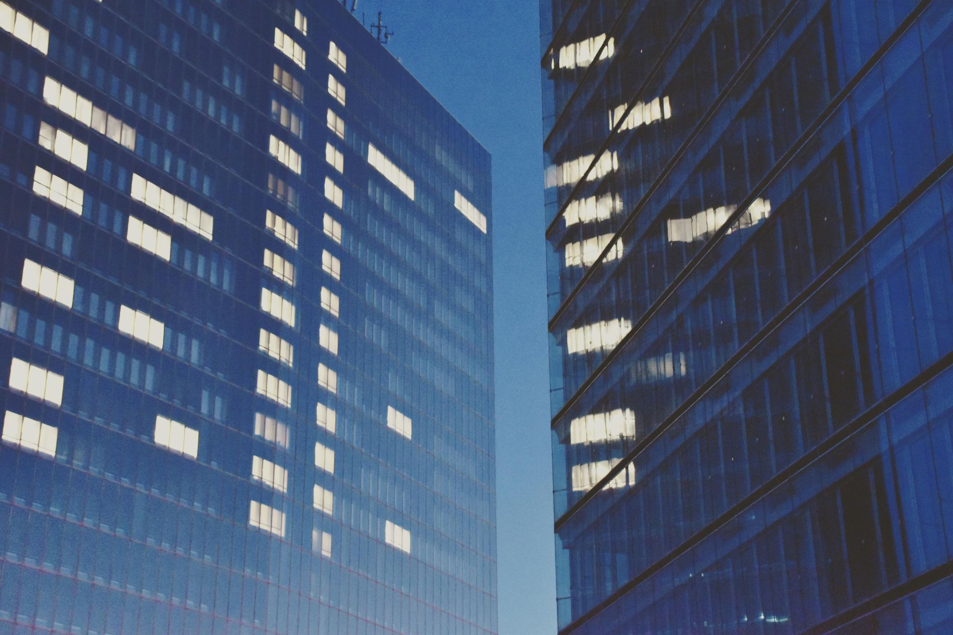 Two tall buildings are lit up at night with a blue sky in the background