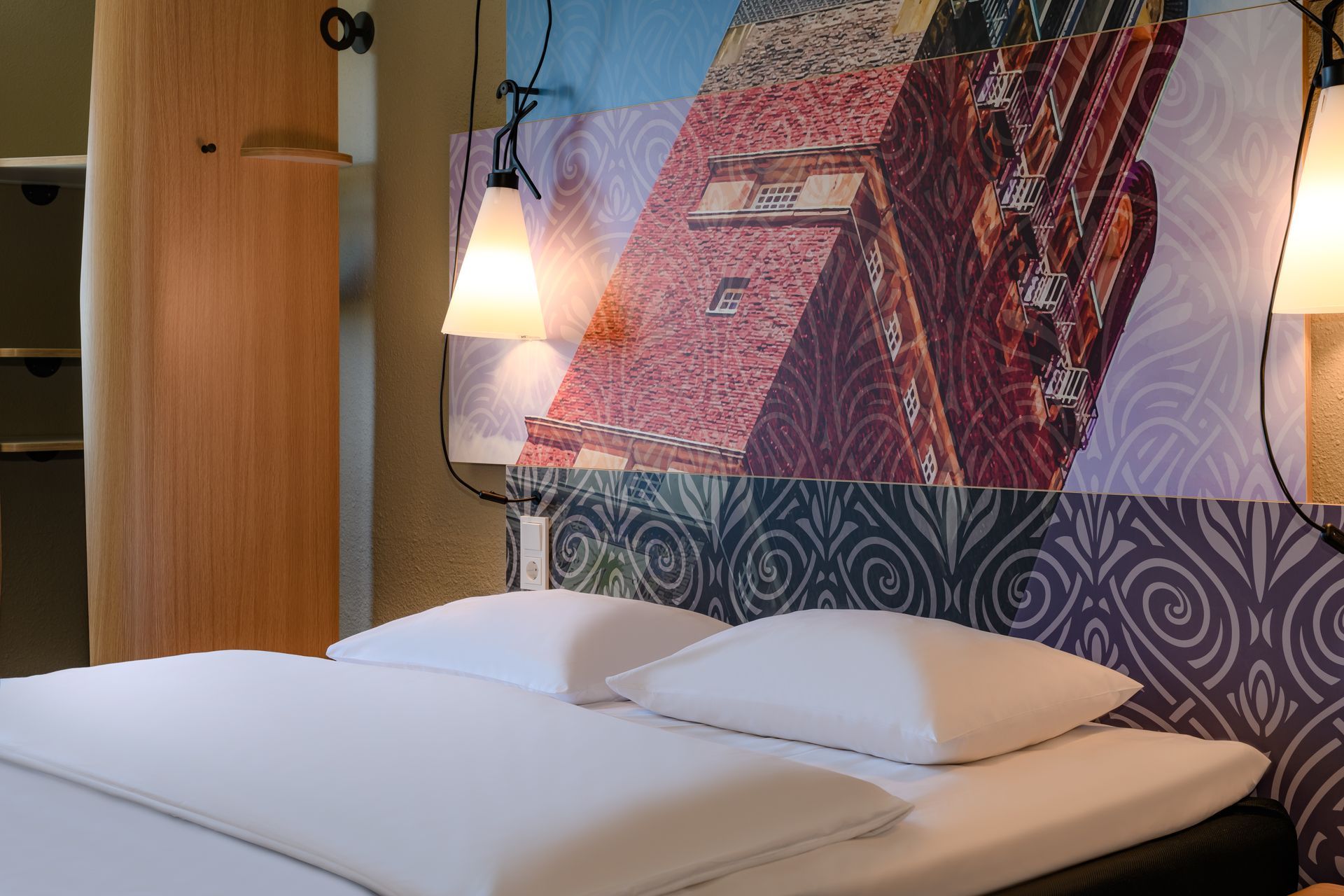 Gemütliches Schlafzimmer mit Doppelbett, gemusterten Wandbildern und Hängelampe unter warmem Licht
