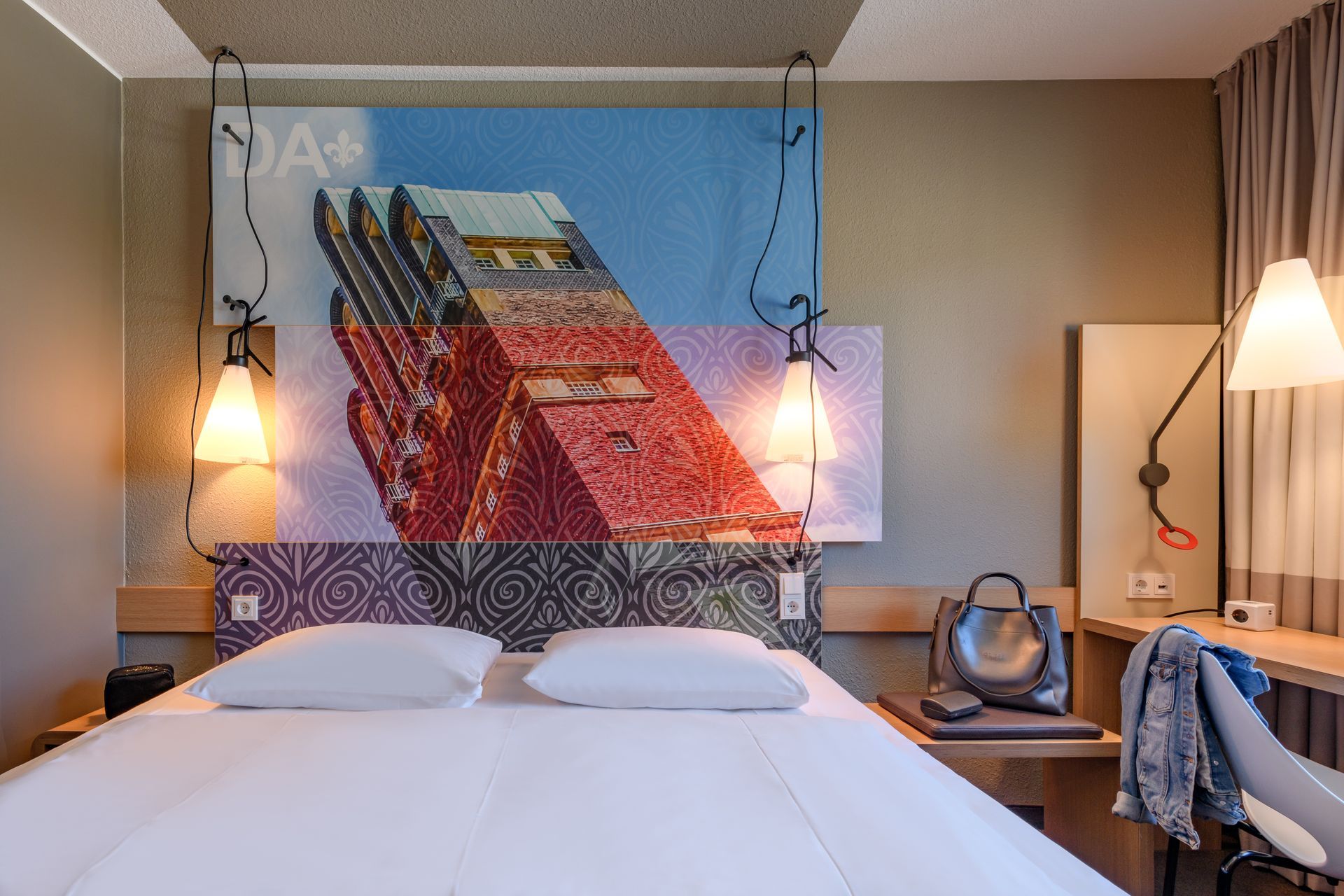 Modern hotel room with a large bed, colorful abstract wall art, bedside lamps, and a desk area