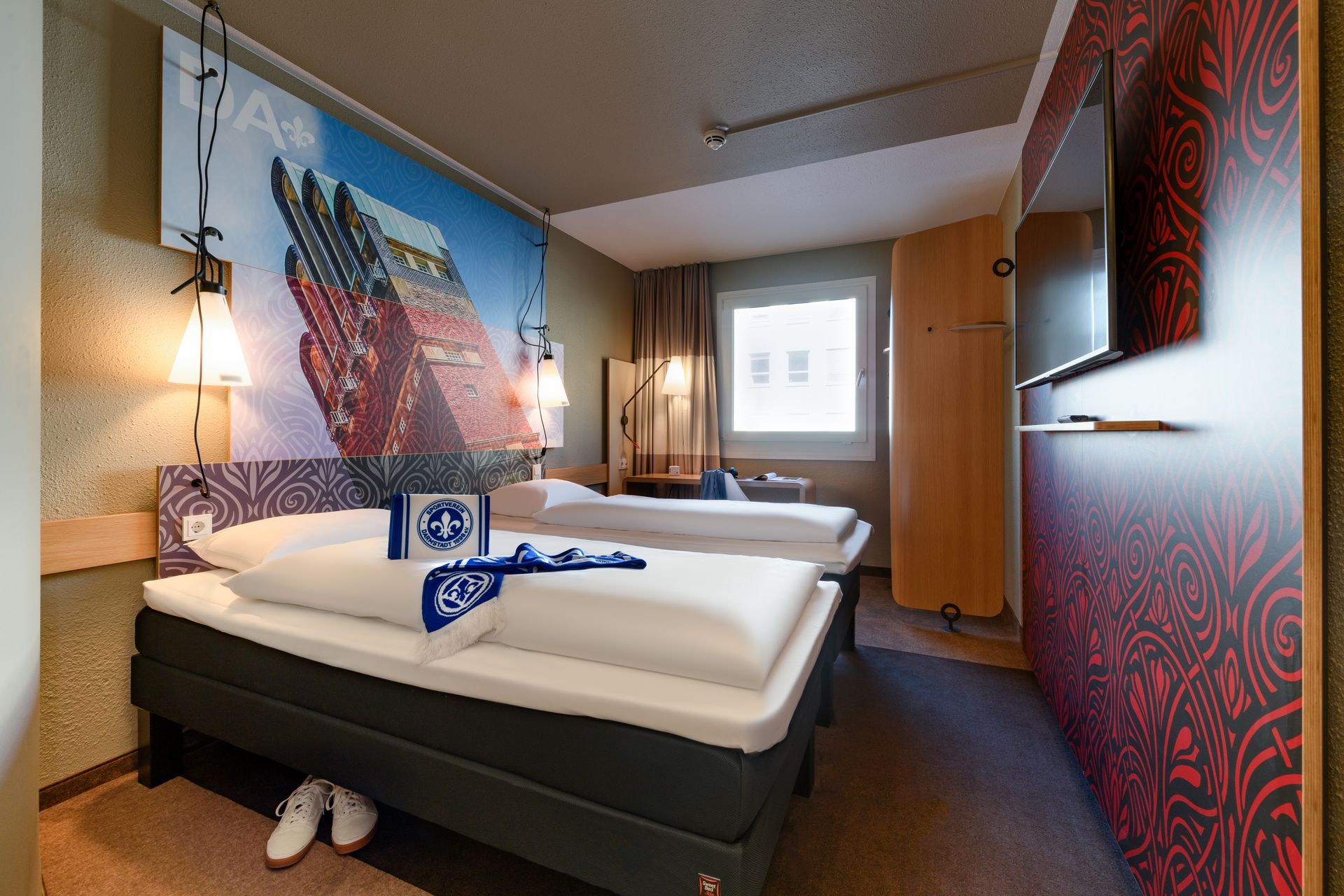 Small hotel room with two twin beds, patterned red walls, and a window at the back