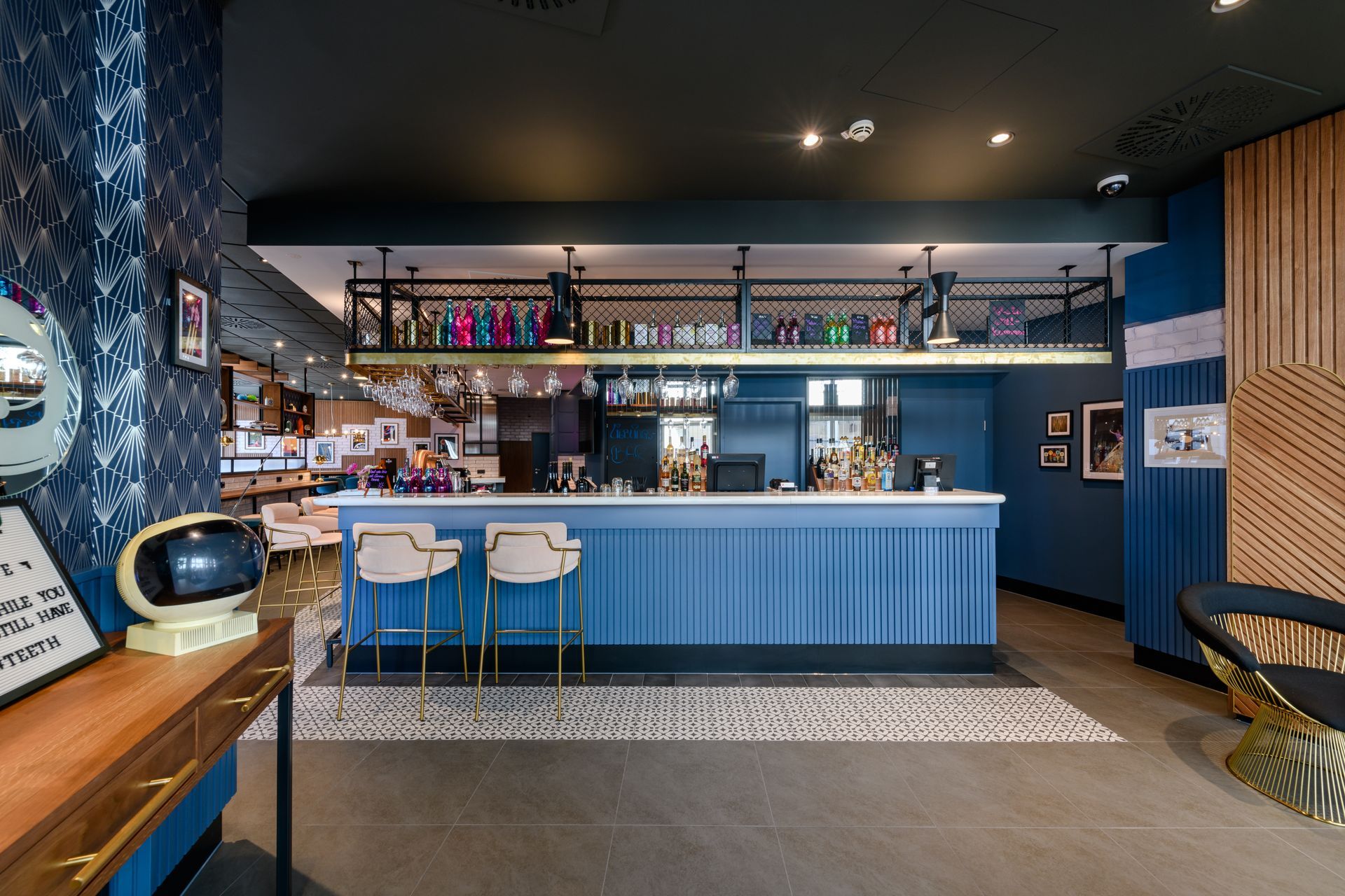 Modern bar interior with blue counter, stools, shelves of bottles, and wood-and-tile decor