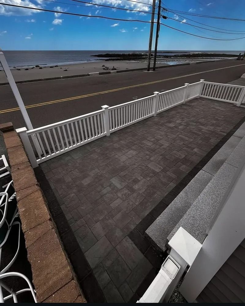 Patio with white railing overlooking a beach and ocean on a sunny day.