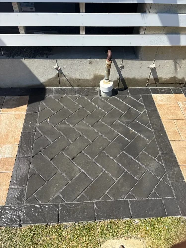 Brick patio with herringbone pattern, black border, near a building with pipes.