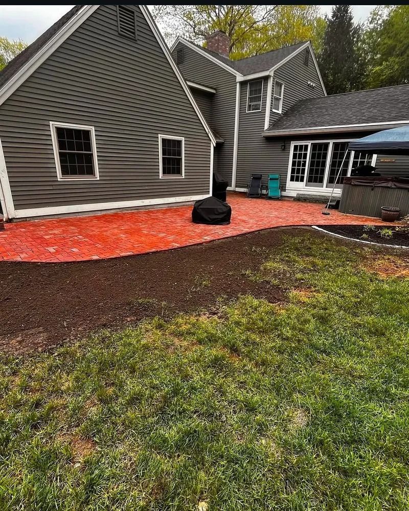 Backyard with a red brick patio, a grey house, and a lawn.