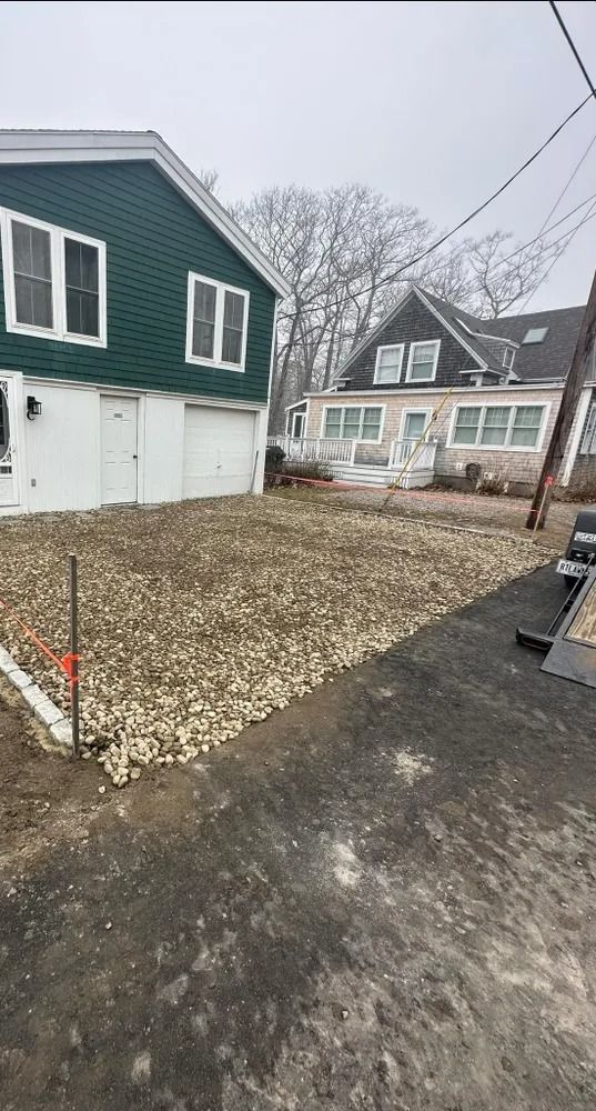 A gravel driveway next to a green house with white garage doors.