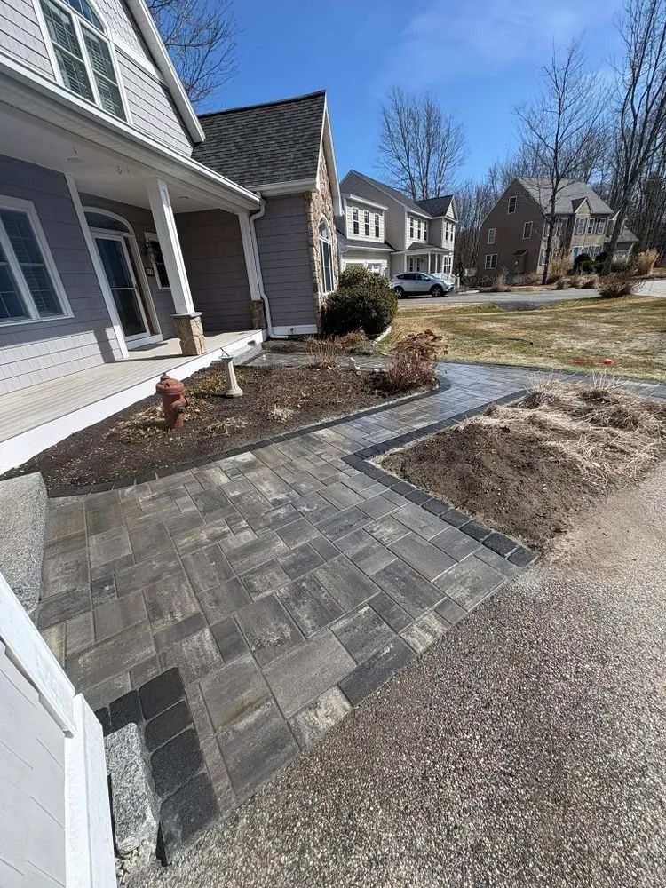 Brick walkway leading to a gray house with a porch, blue sky.