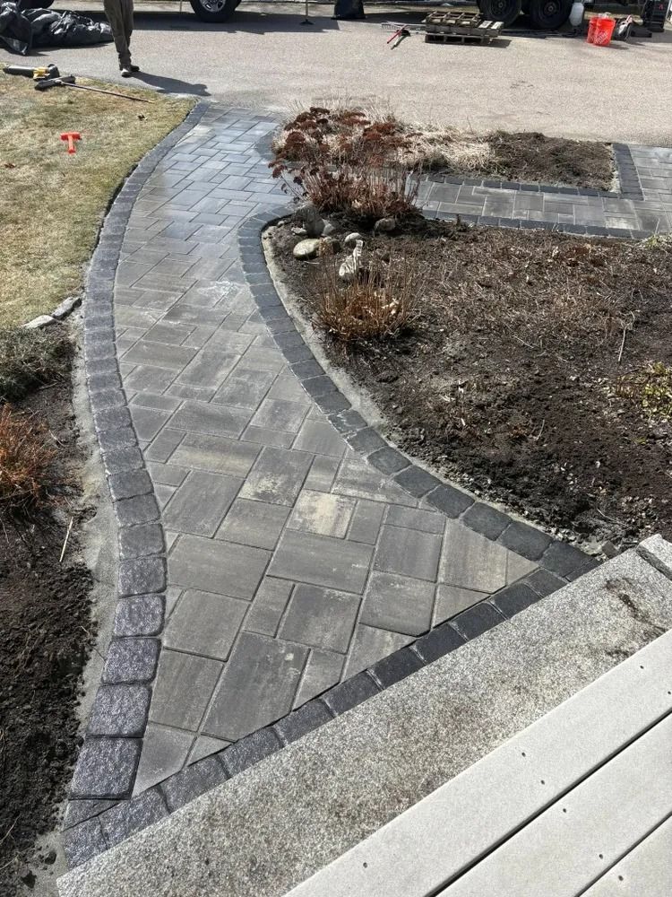 Stone pathway curves through a yard, bordered by dark gray pavers and edged with plants.
