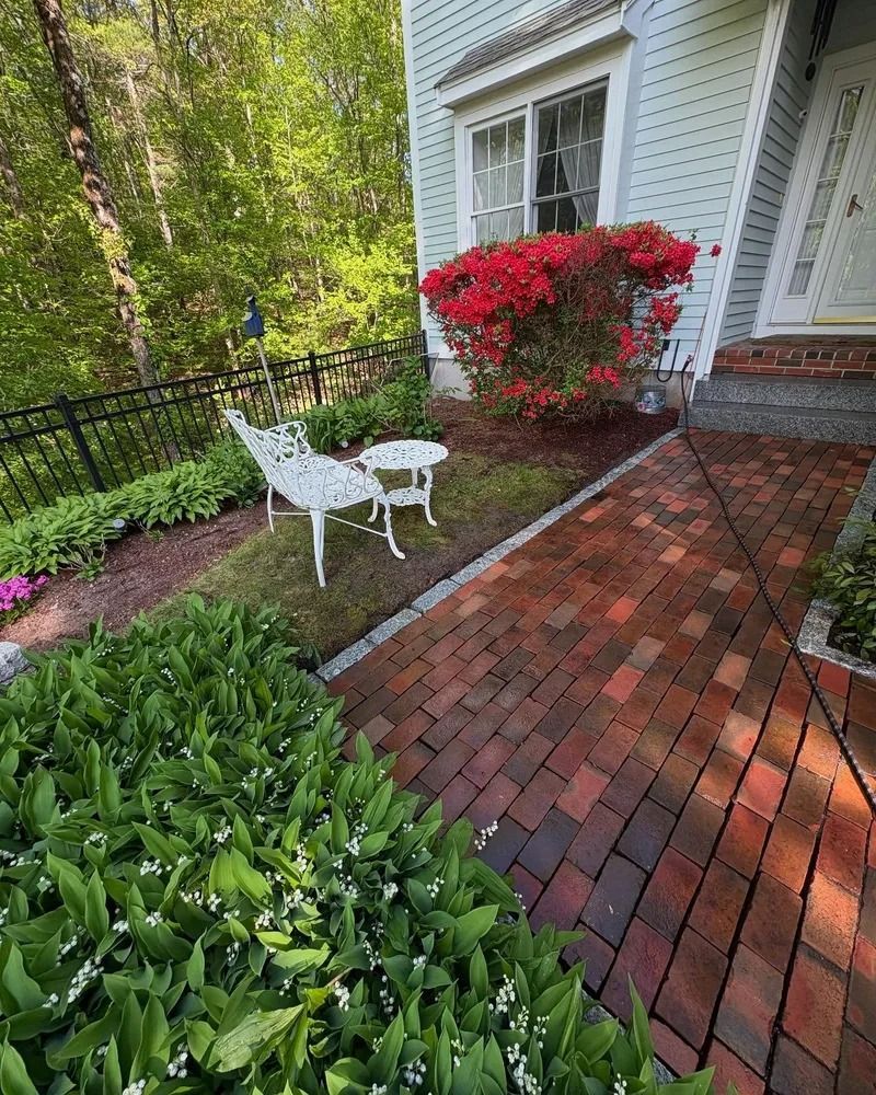 Brick path leading to a house with red azalea bushes and white garden furniture.