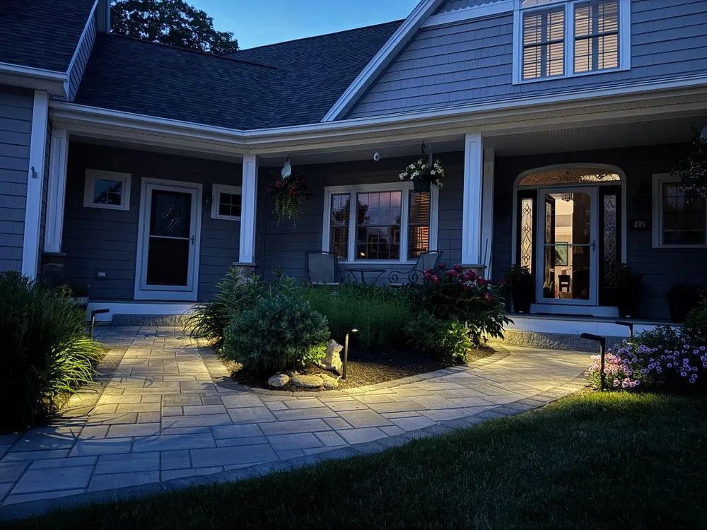 A house at dusk with path lighting illuminating a stone walkway and front porch with plants.