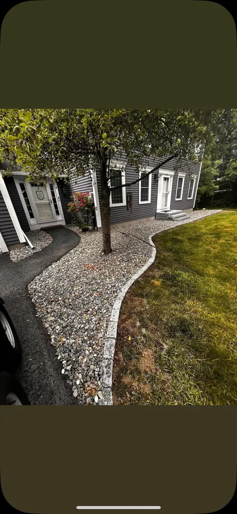 A gray house with white trim, a gravel path, and a tree in the center.