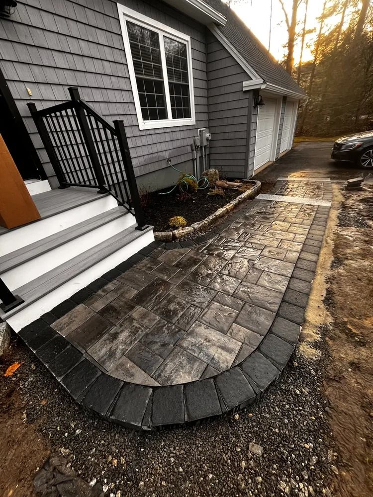 Brick walkway leading to a house entrance with gray siding and a black railing.