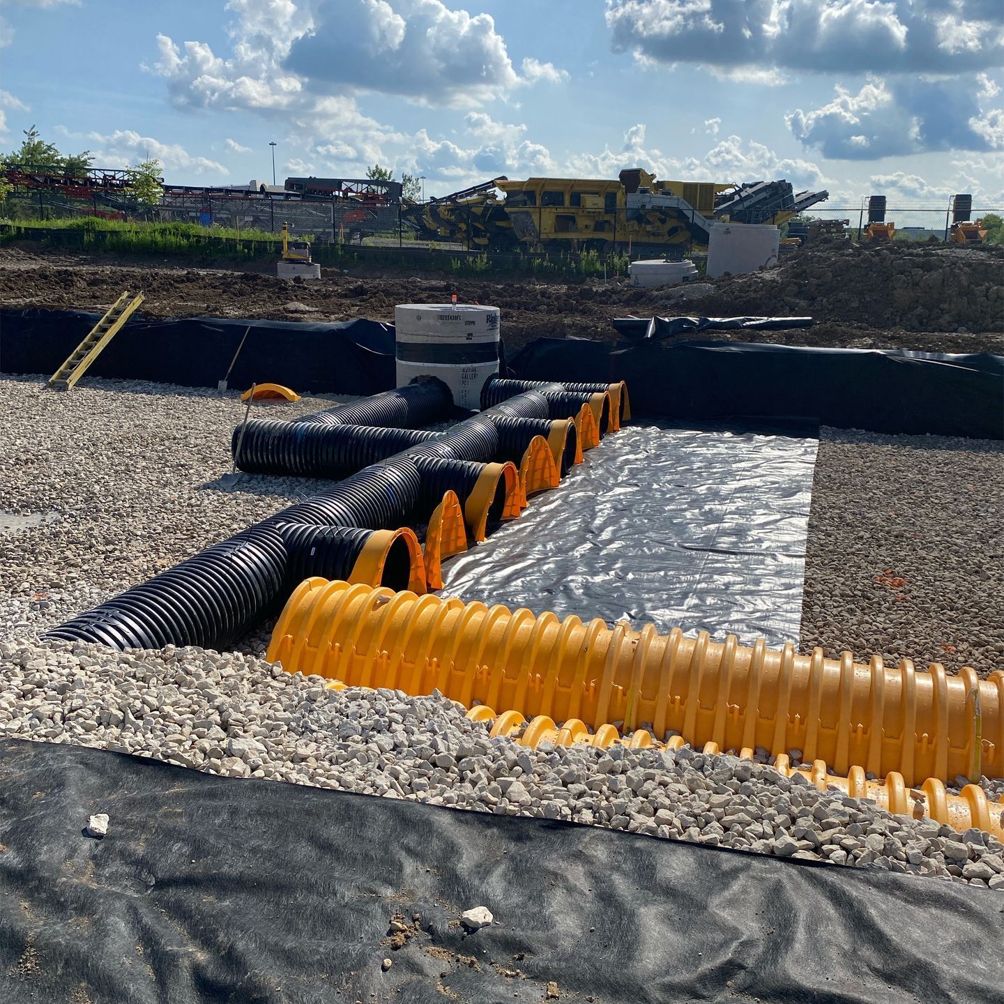 A bunch of yellow pipes are sitting on top of a gravel road.