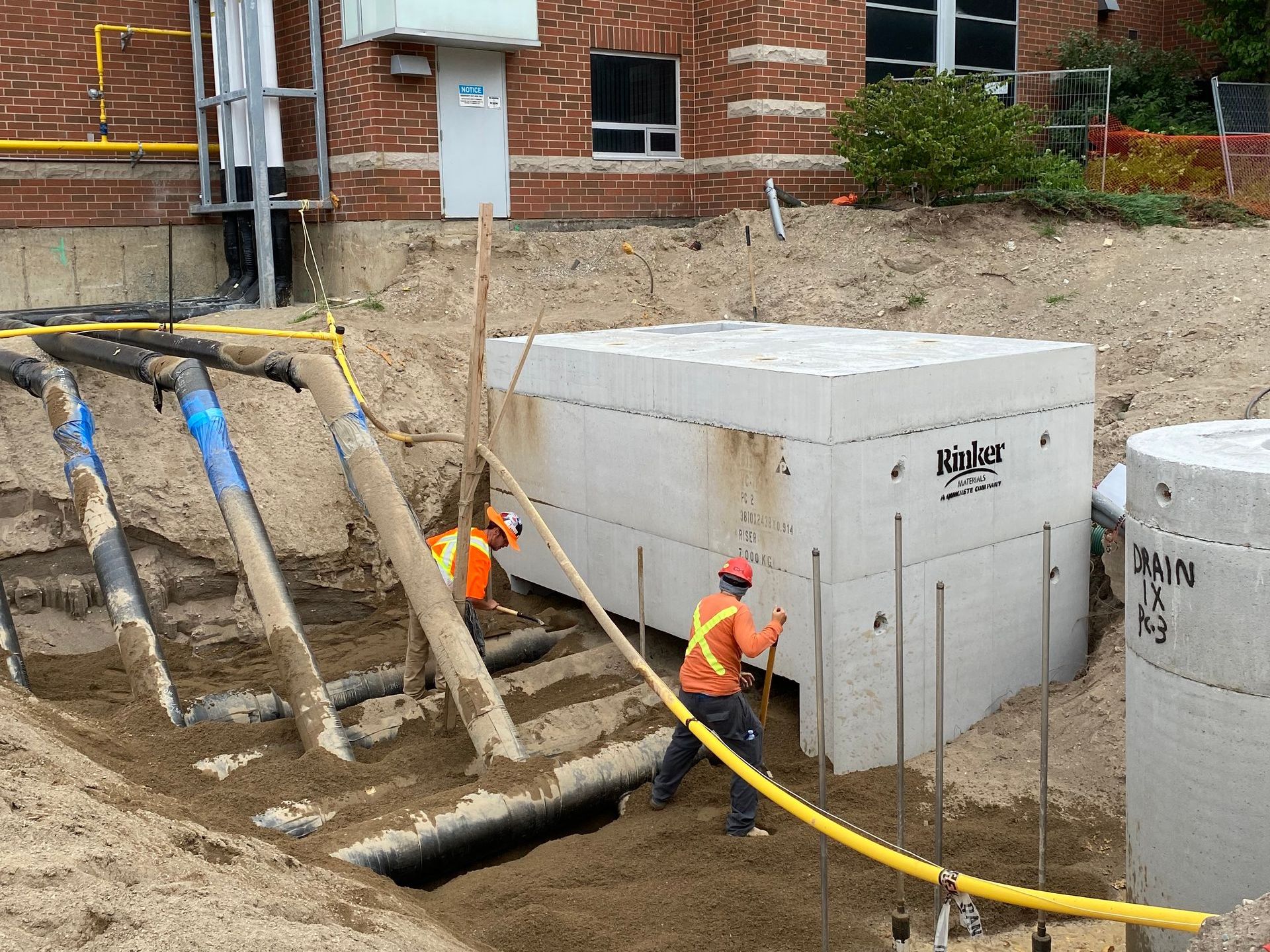 Two construction workers are working on a construction site in front of a brick building.