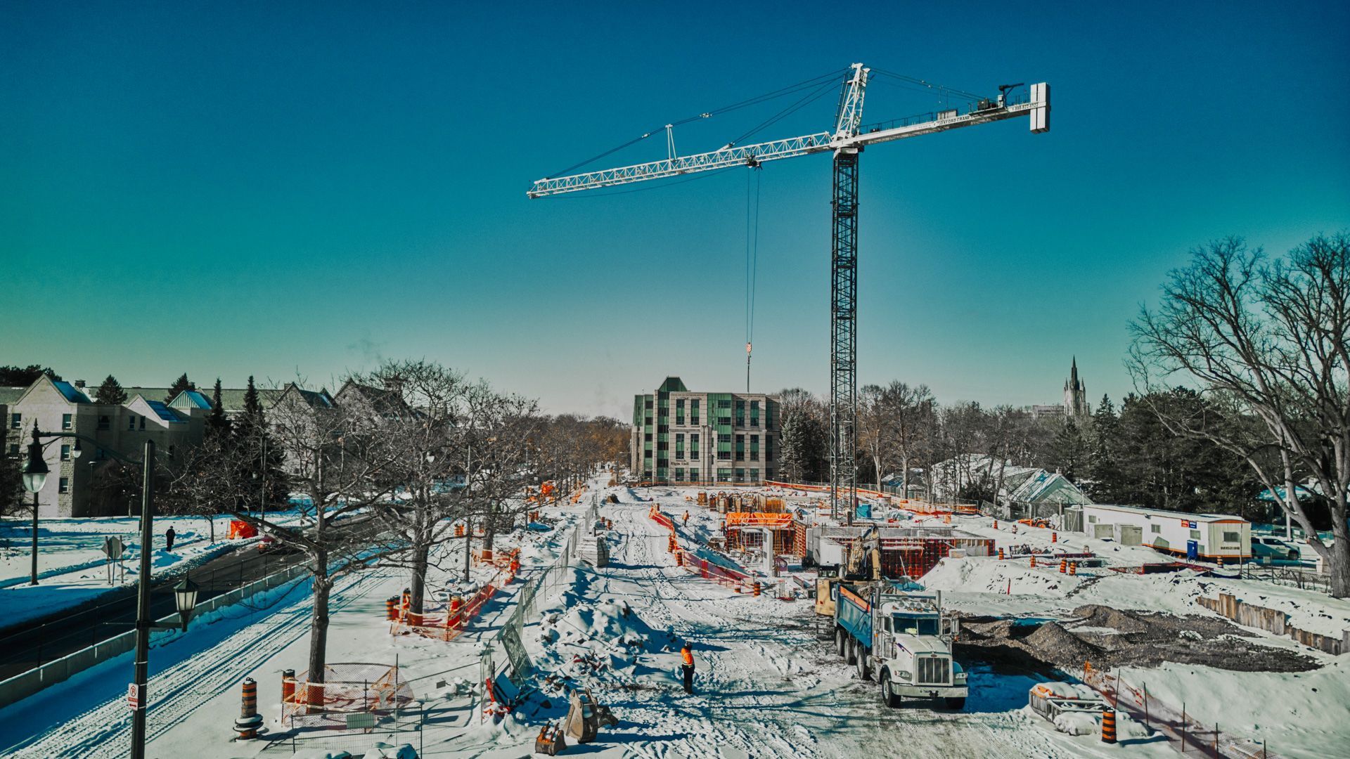 A construction site in the snow with a crane in the foreground.