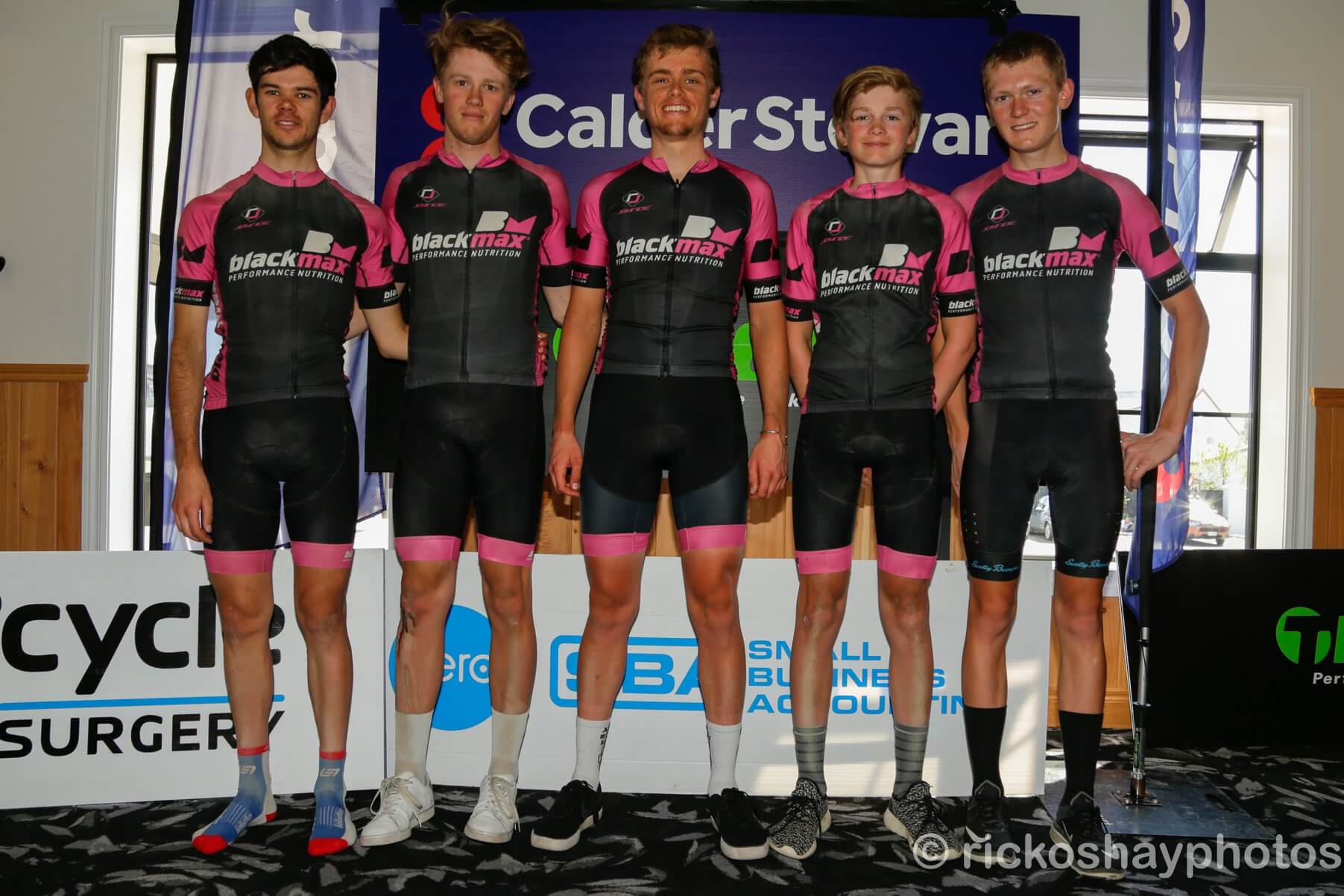 A group of young men are standing in front of a sign that says cycle surgeon