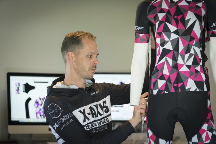 A man is kneeling down in front of a mannequin wearing a pink and black shirt.