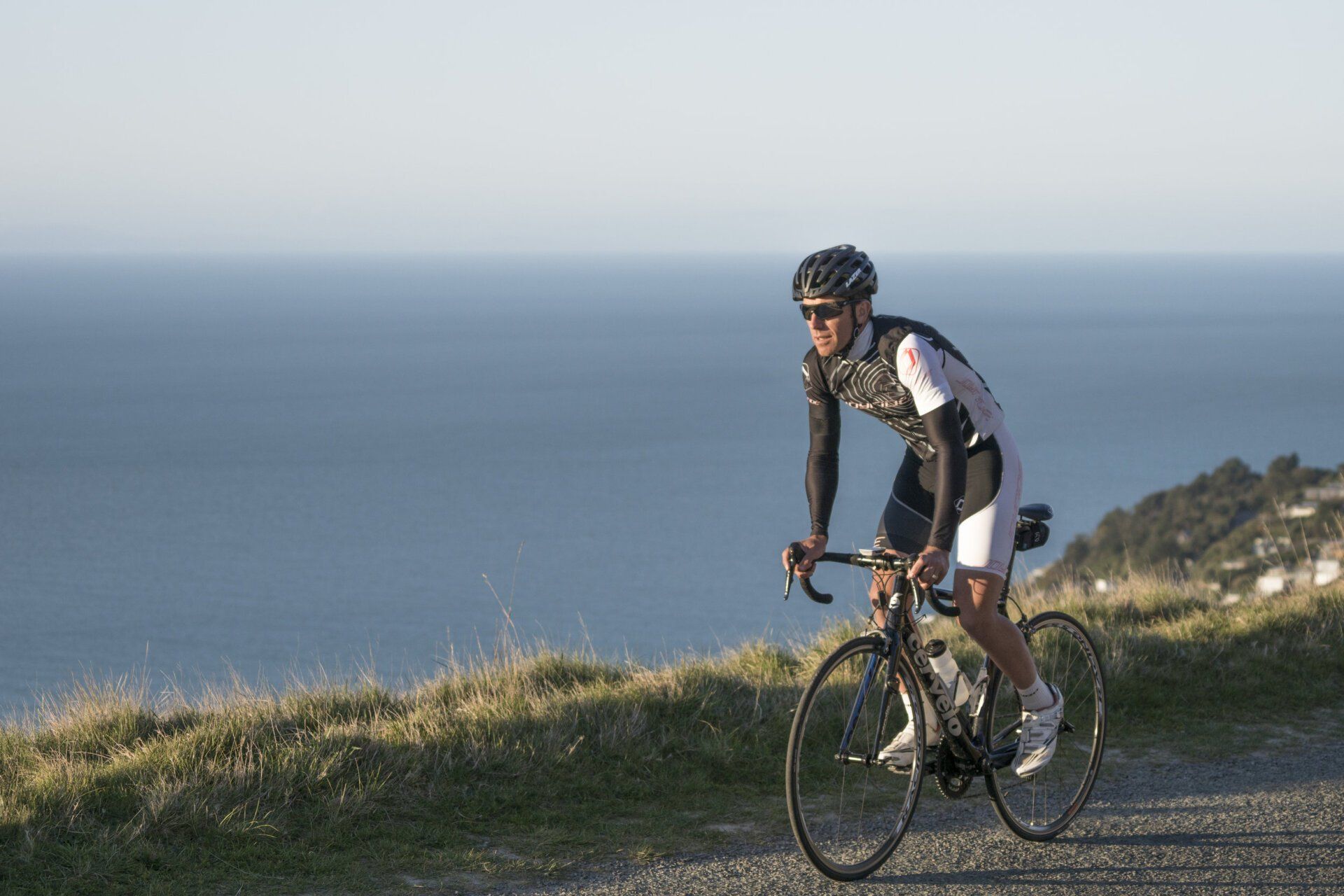 A man is riding a bike on a dirt road near the ocean.