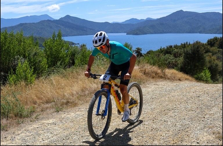 A man is riding a bike on a dirt road with a lake in the background