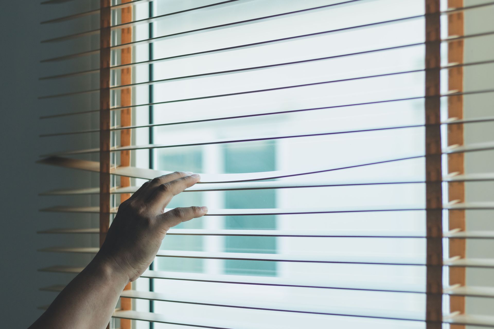 A person is opening a window with blinds on it.