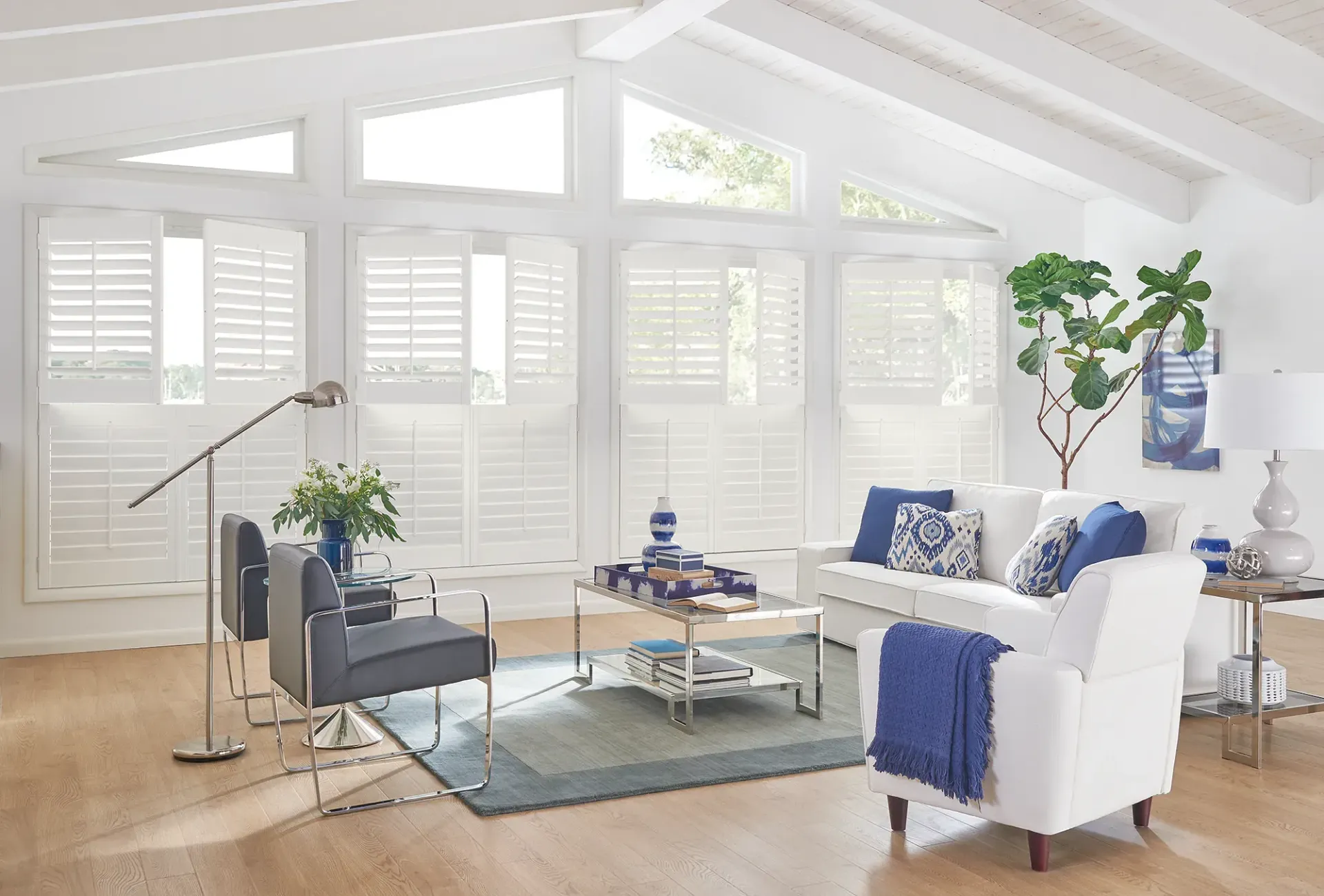 A living room with a couch , chairs , coffee table and shutters on the windows.