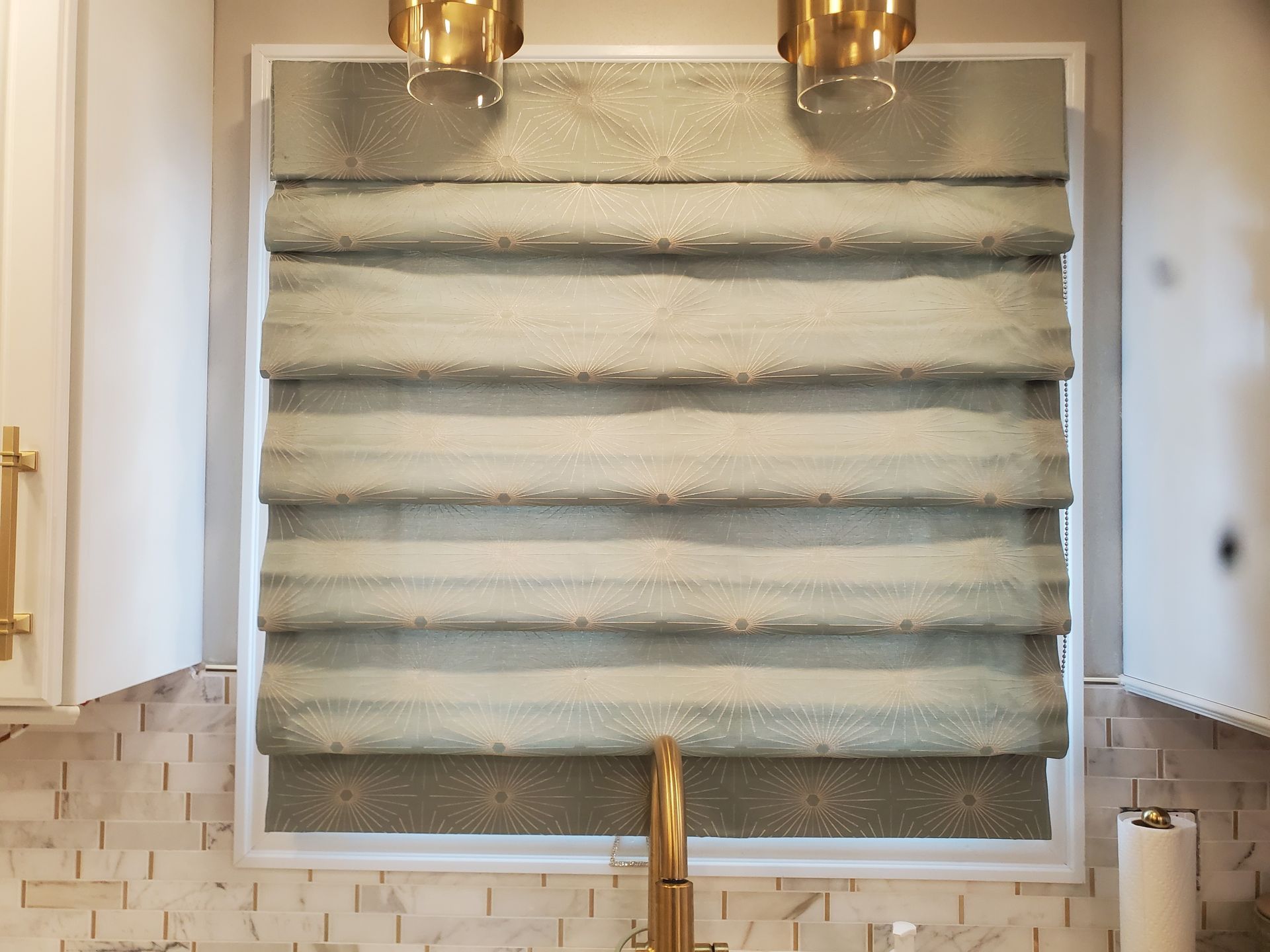 A kitchen window with a roman shade and a sink.
