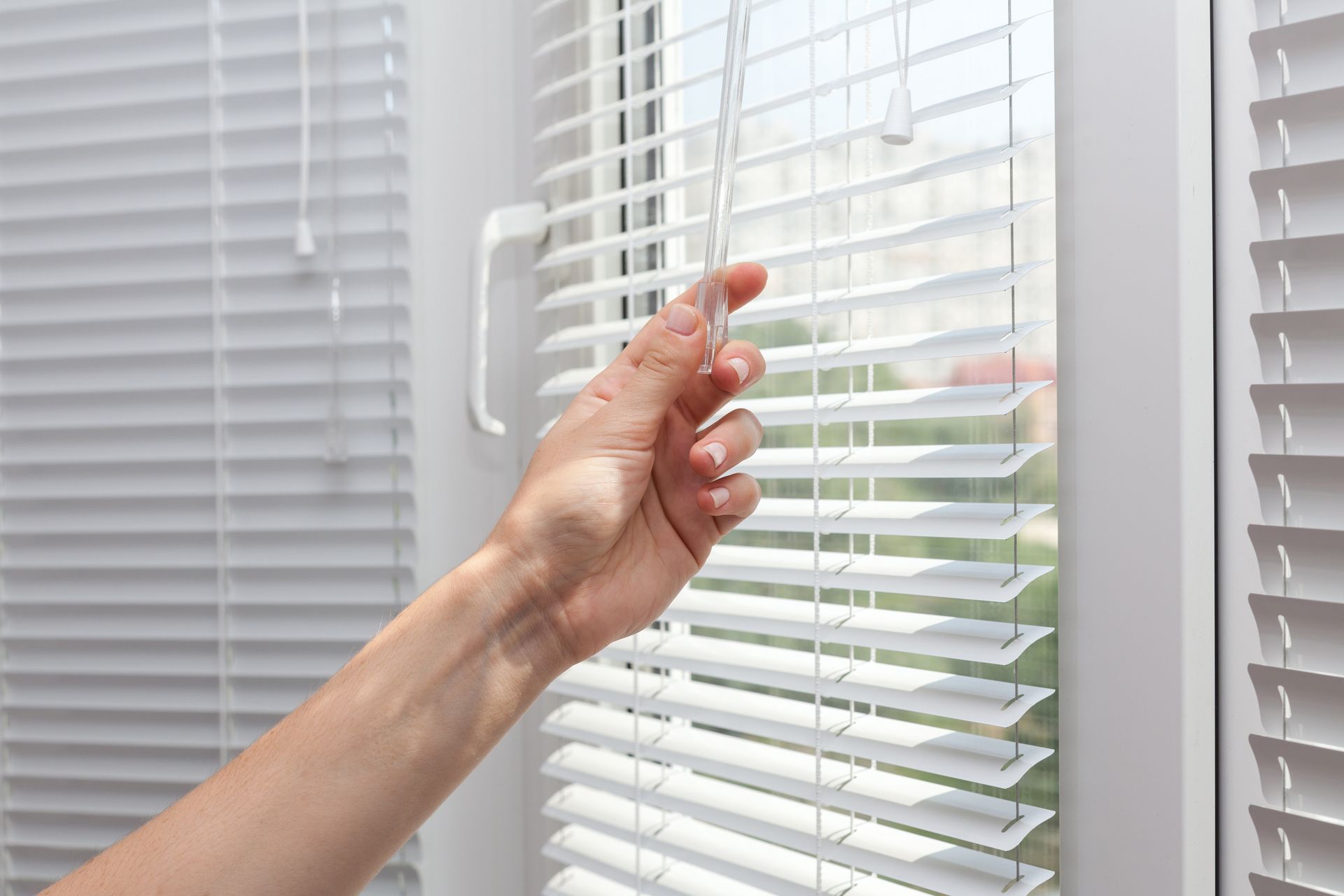 A person is opening a window with blinds on it.