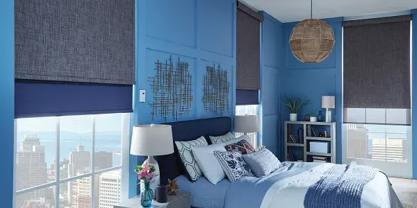 A bedroom with blue walls , a bed , lamps , and a window.