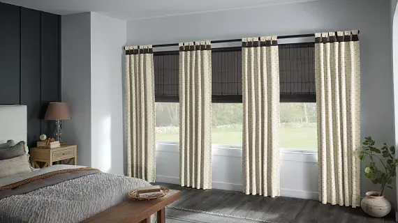 A bedroom with a bed , curtains , and roman shades.