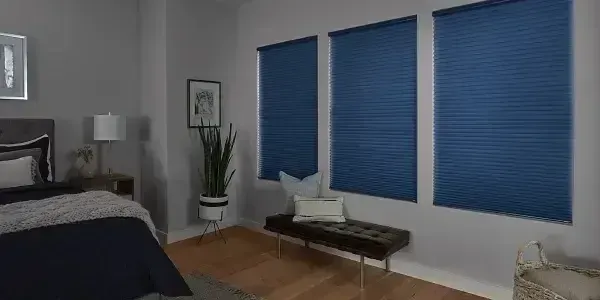 A bedroom with three blue blinds on the windows and a bed.