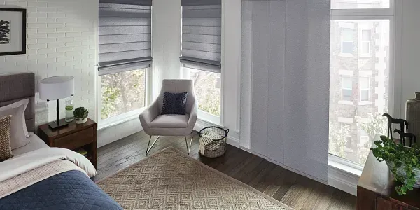 A bedroom with a bed , chair , nightstand and two windows.