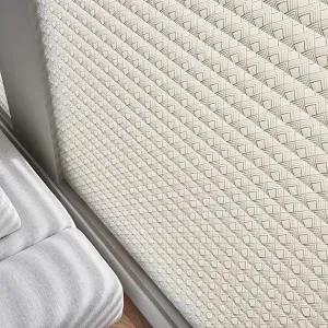 A close up of a white blind on a window next to a bed.