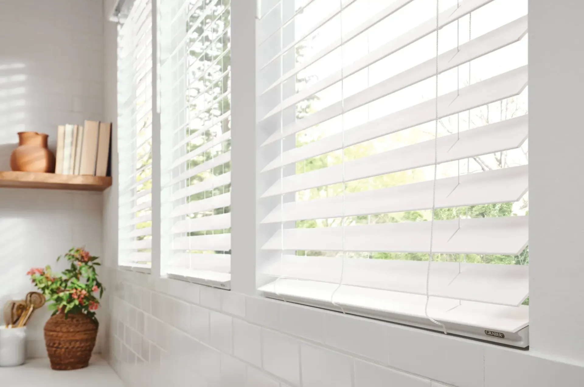 A kitchen with white blinds on the windows and a vase of flowers on the counter.