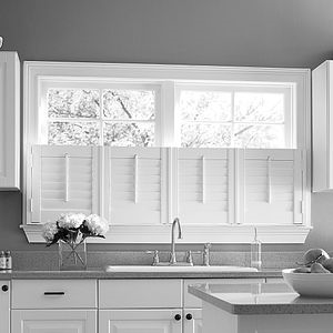 A black and white photo of a kitchen with white cabinets , a sink , and a window.