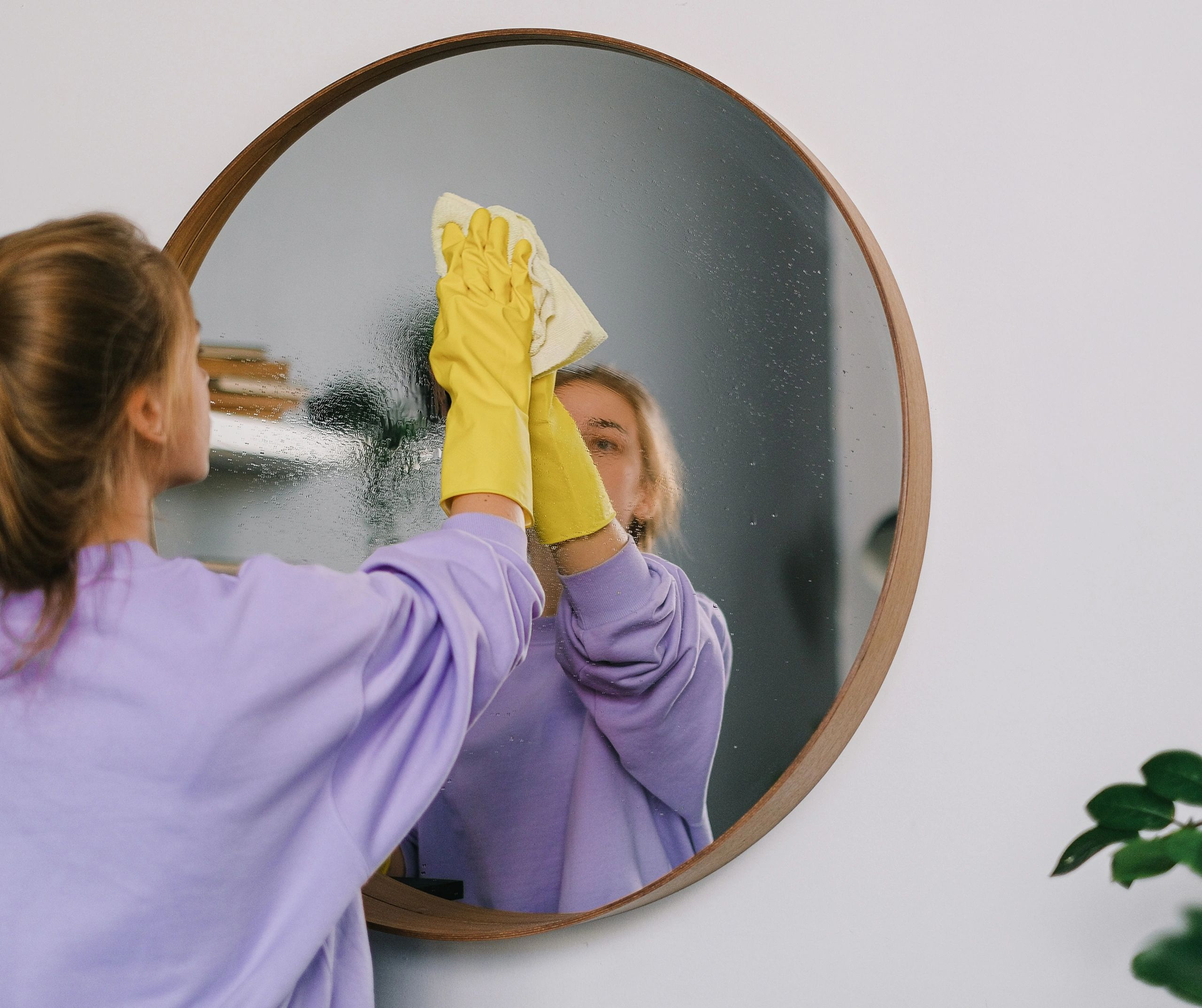 A woman is cleaning a mirror with a cloth and gloves.