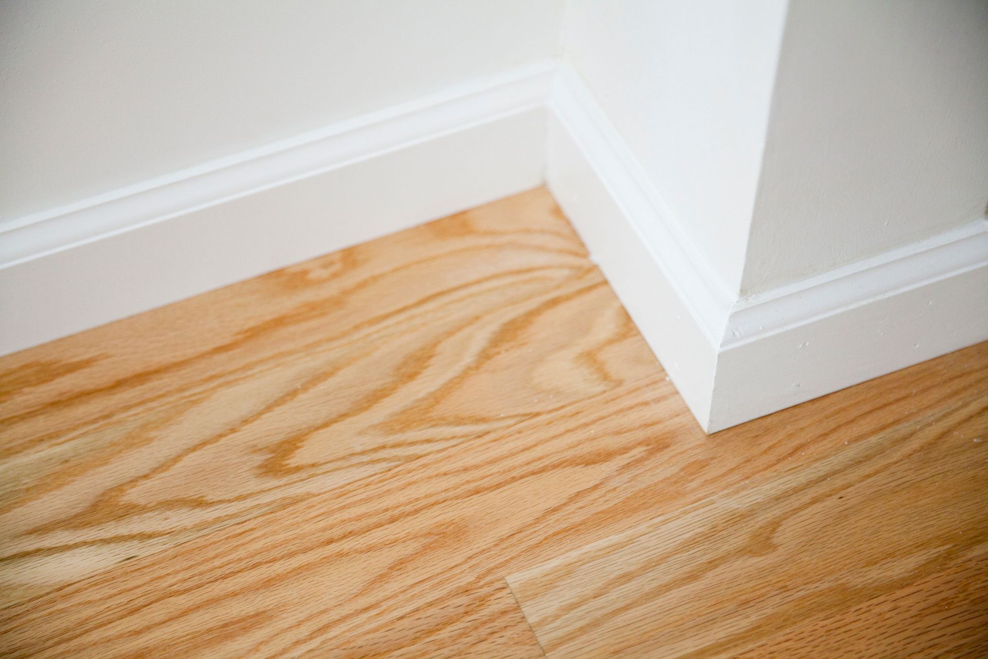 A close up of a wooden floor with white molding and a white wall.