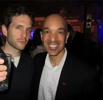 Two men are posing for a picture and one is holding a glass