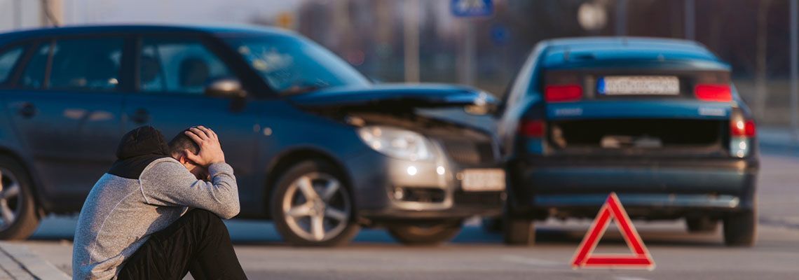 A woman is sitting in front of a car that has crashed into another car.