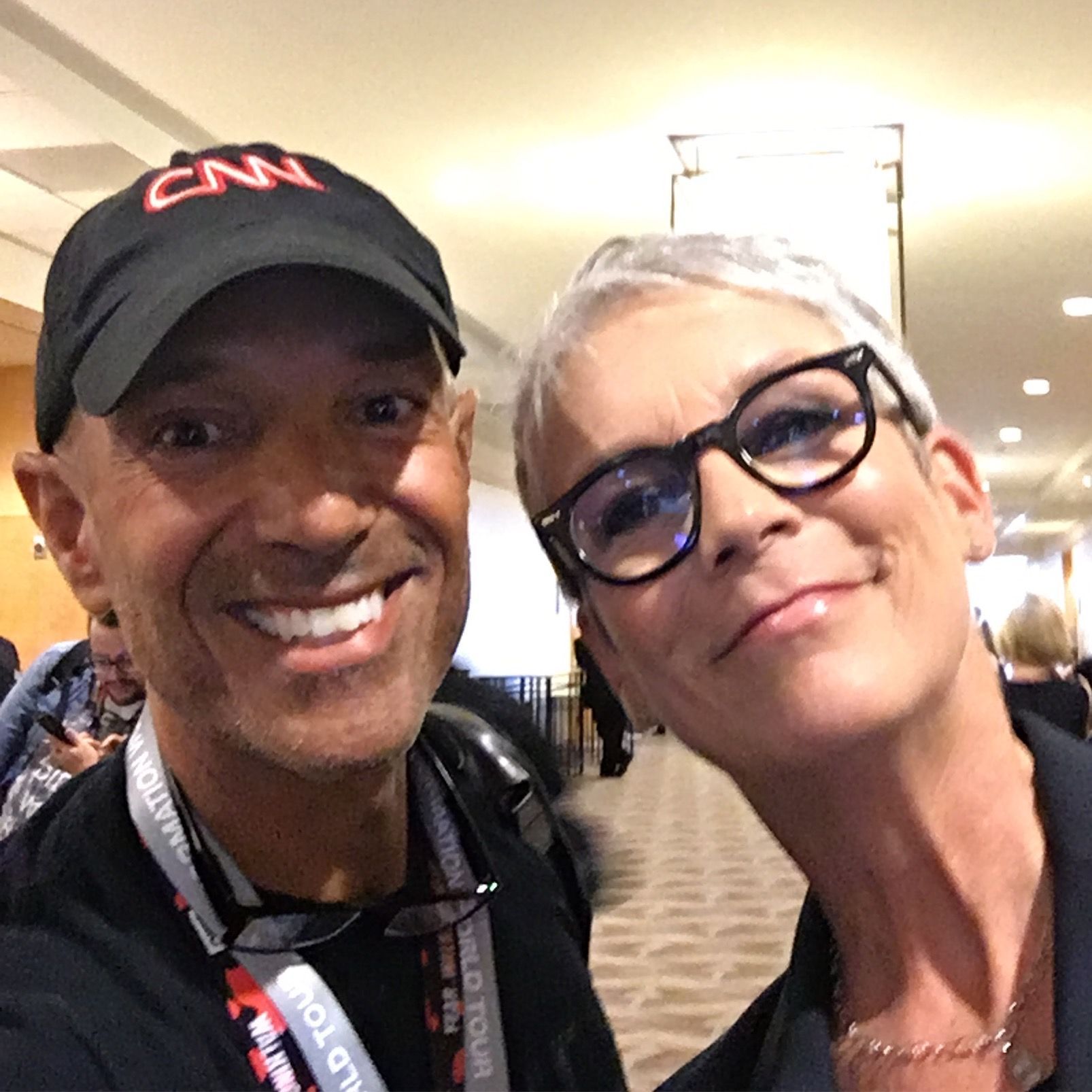 A man wearing a cnn hat poses with a woman wearing glasses