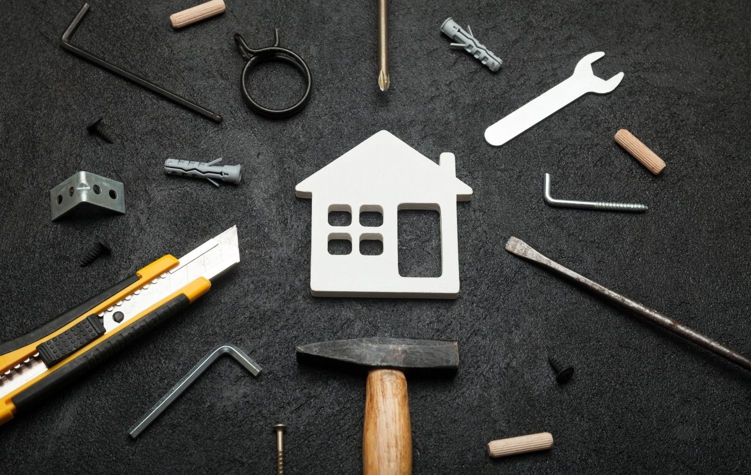 White house model surrounded by tools on black surface, symbolizing home improvement.