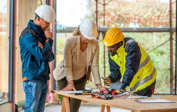 Two people shaking hands over blueprints and miniature house models.