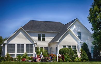 White two-story house with a dark roof and a lush green lawn on a sunny day.