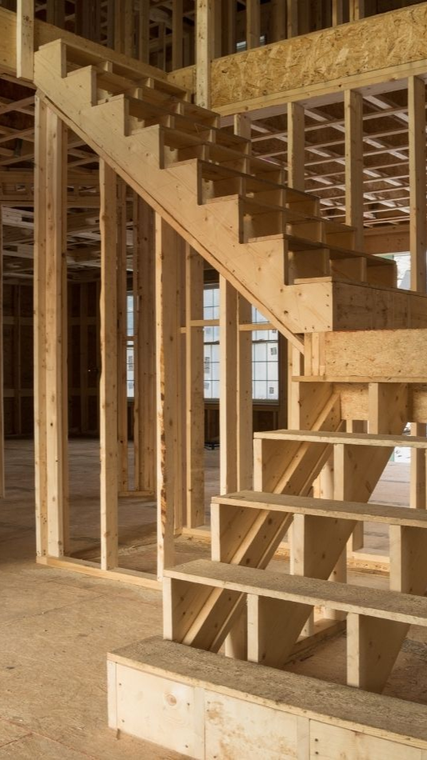 Framed wooden staircase in a house under construction; steps, stringers, and supports visible.