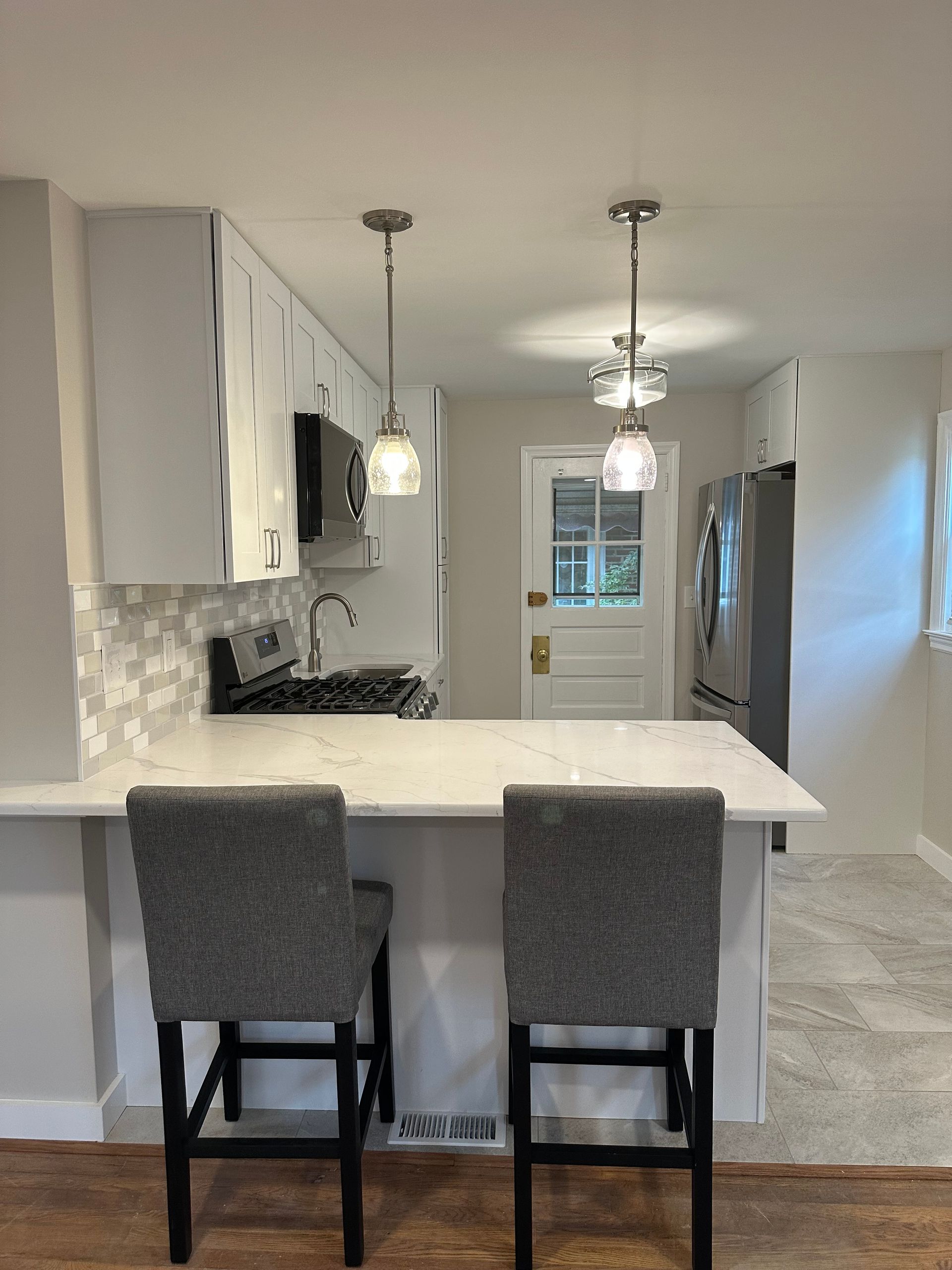 Modern kitchen with a white island, two gray bar stools, and pendant lights.