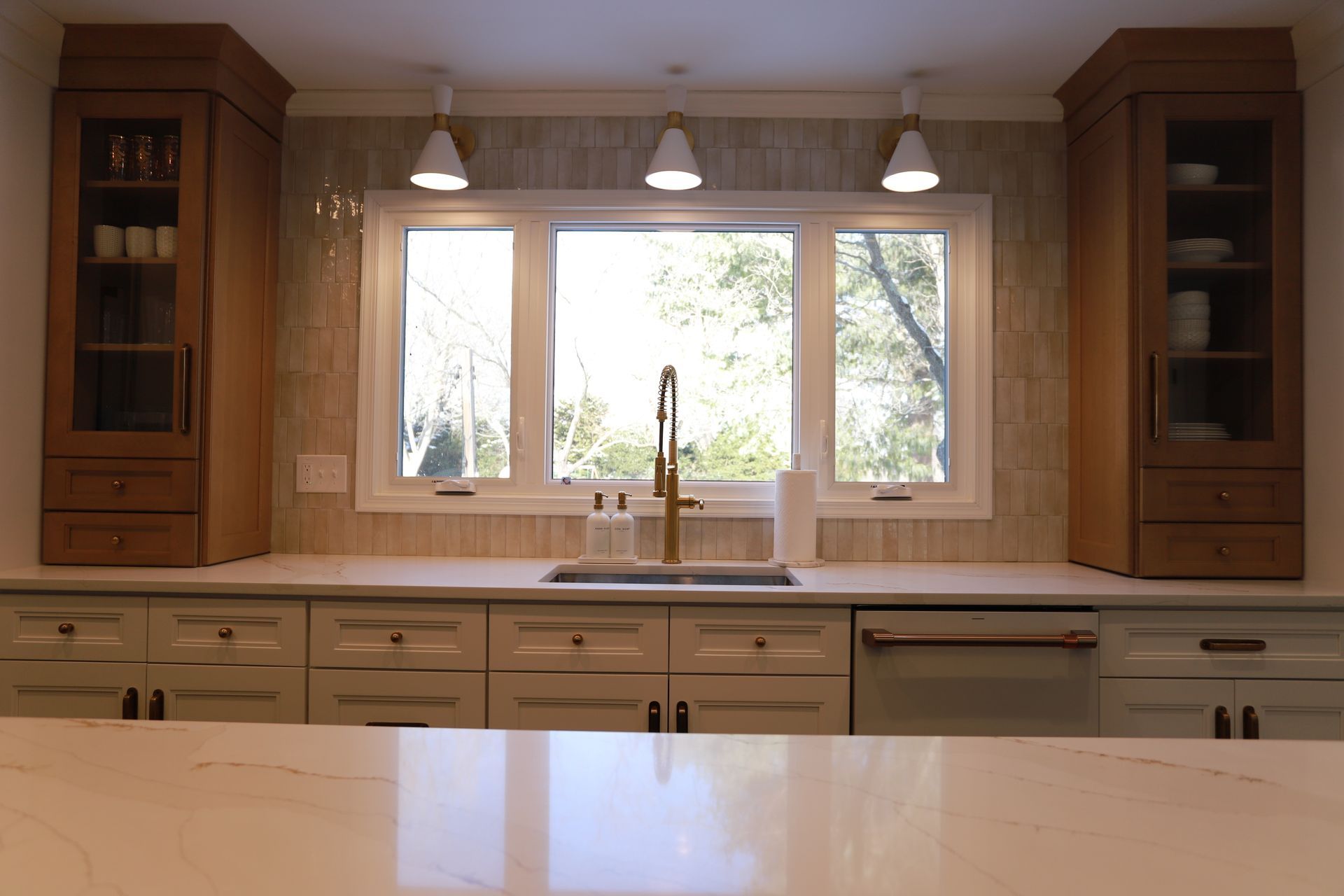 Modern kitchen with wooden cabinets, double window, farmhouse sink, and white island countertop.