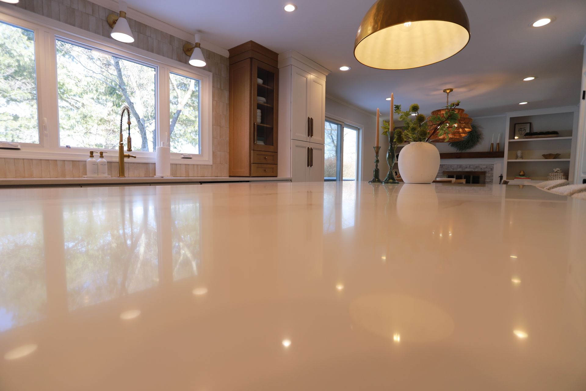Modern open-plan kitchen with glossy white floor, pendant lights, windows, and a vase centerpiece