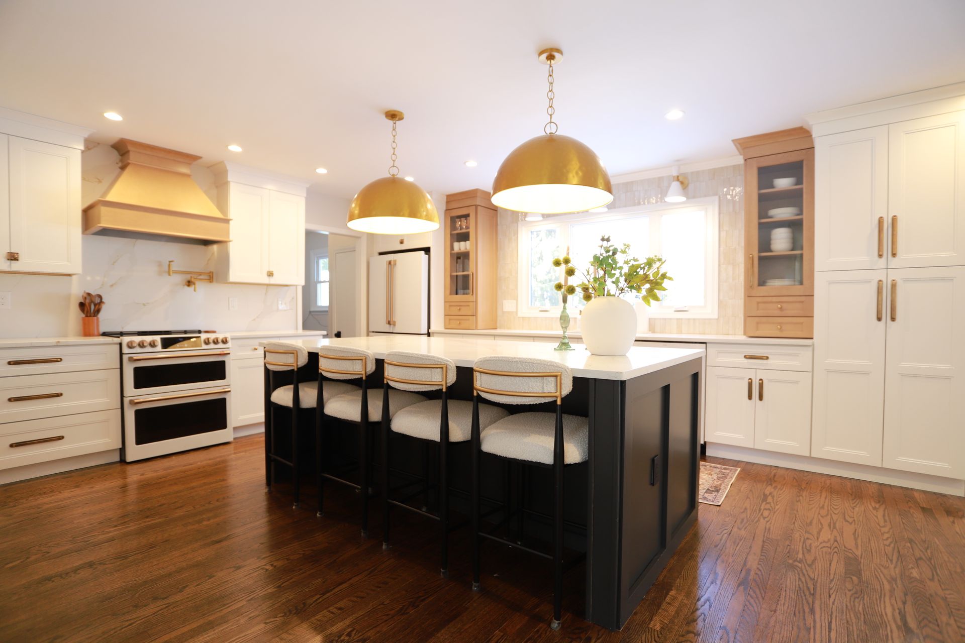 Bright modern kitchen with white cabinets, black island, gold pendant lights, and hardwood floors