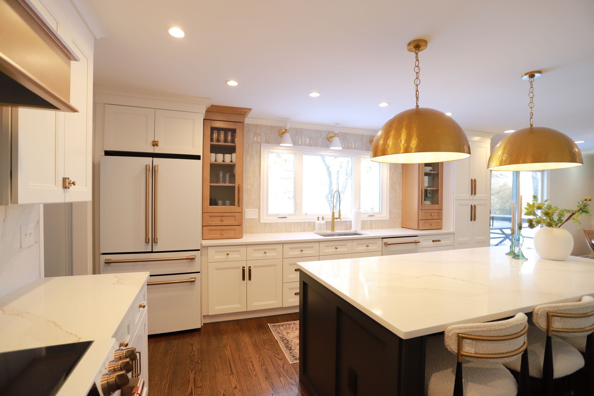 Bright white kitchen with island, gold pendant lights, hardwood floor, and windows letting in daylight