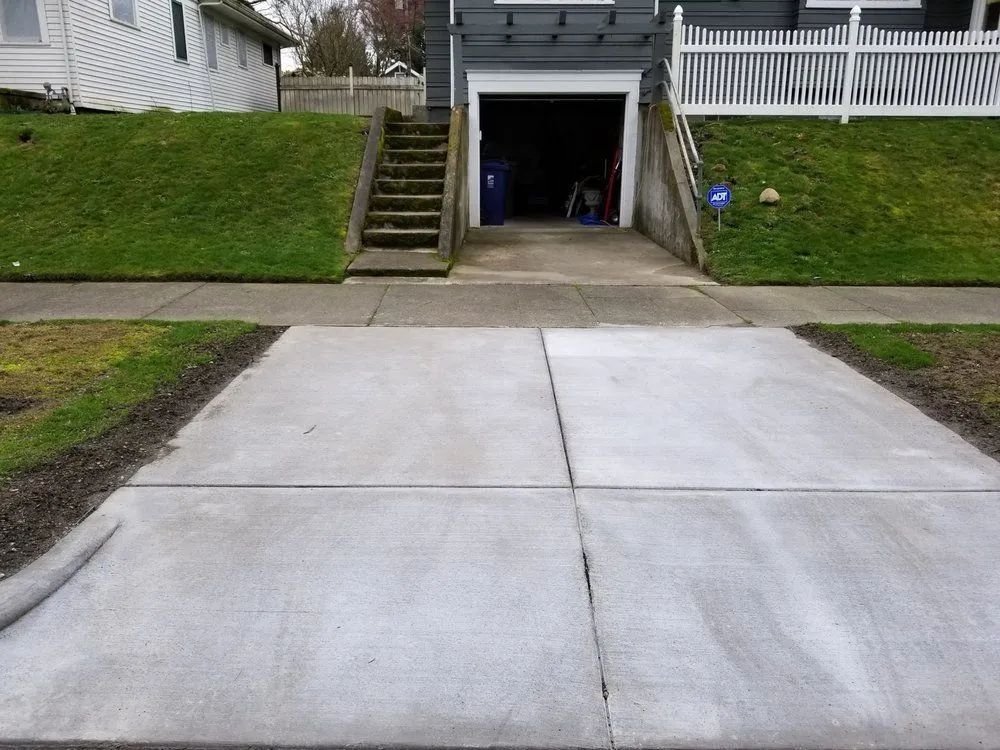 Concrete driveway leading to an open garage between two grassy embankments and stairs.