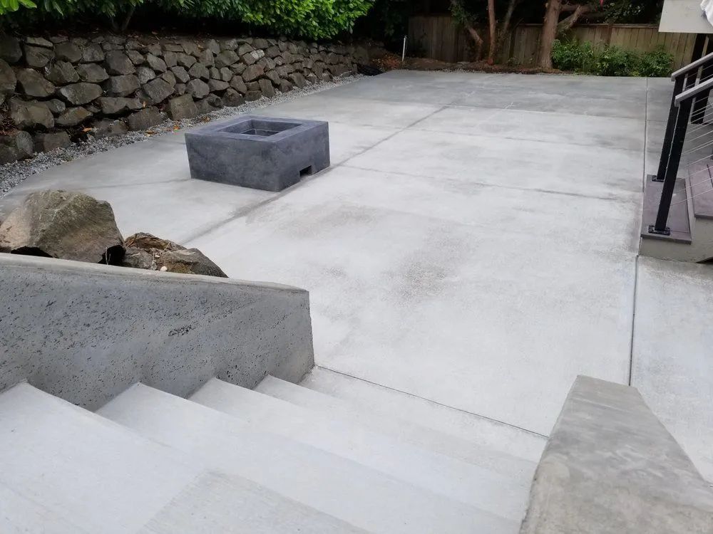 Concrete outdoor steps leading to a wide patio with stone wall and low block benches