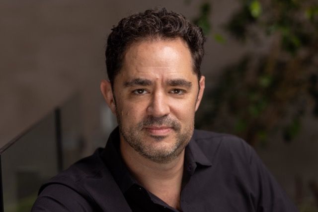A man with a beard is wearing a black shirt and looking at the camera.